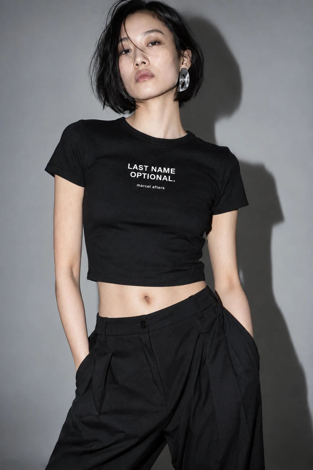 Adult female model wearing the black Marcel Afters Last Name Optional shirt with white lettering.