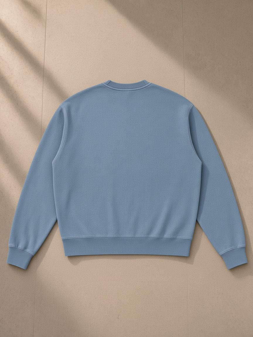 Unisex vintage wash crewneck sweatshirt in Jeans Blue, laid flat on pale limestone, back view