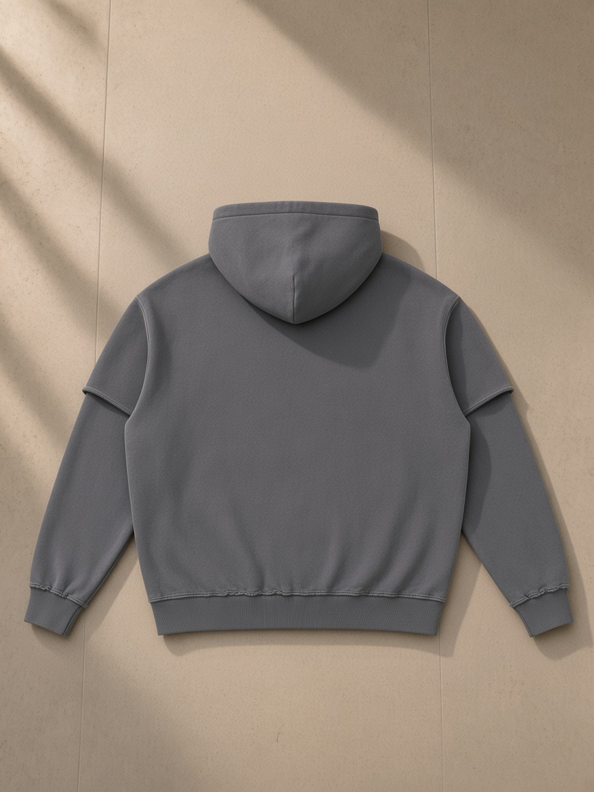 Snow washed raw edge double layered hoodie in Dark Gray, laid flat on pale limestone, back view
