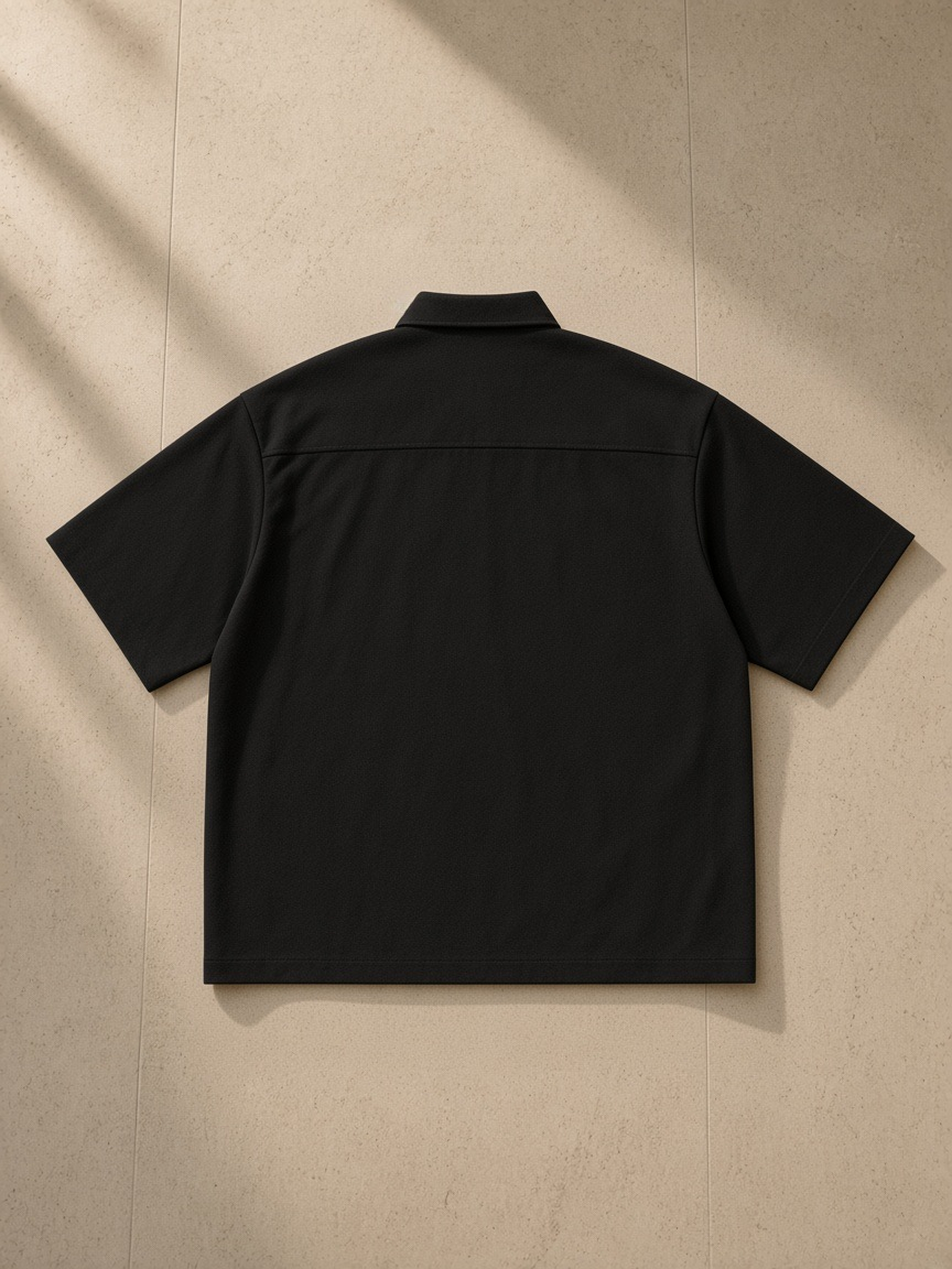 Boxy Heavyweight Short Sleeve Shirt — Dark in Black, laid flat on pale limestone, back.