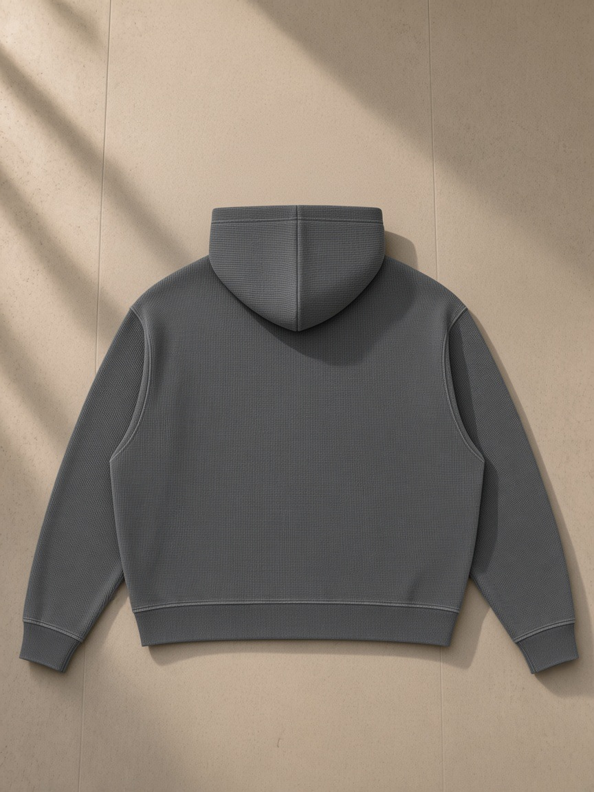 Unisex vintage wash boxy waffle full zip hoodie in Dark Gray, laid flat on pale limestone, back view