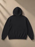Unisex oversize heavyweight fleece hoodie in Black Beauty, laid flat on pale limestone, back view