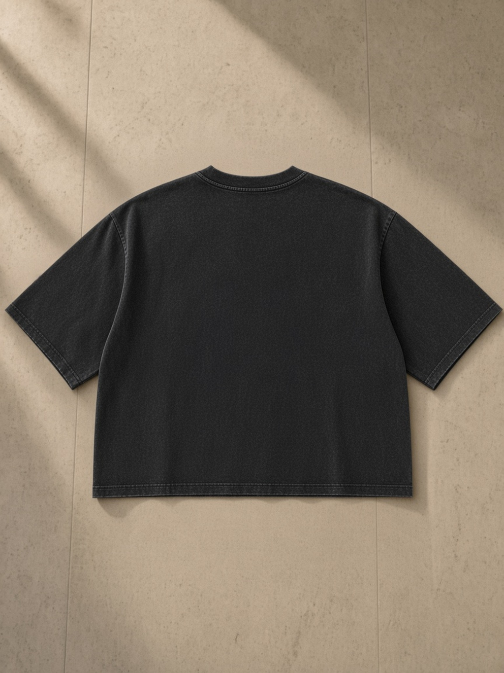 Mineral Wash Raw Hem Boxy T-Shirt in Black, laid flat on pale limestone, back.