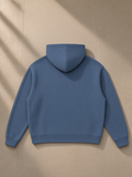 Unisex waffle boxy full zip hoodie in Jeans Blue, laid flat on pale limestone, back view