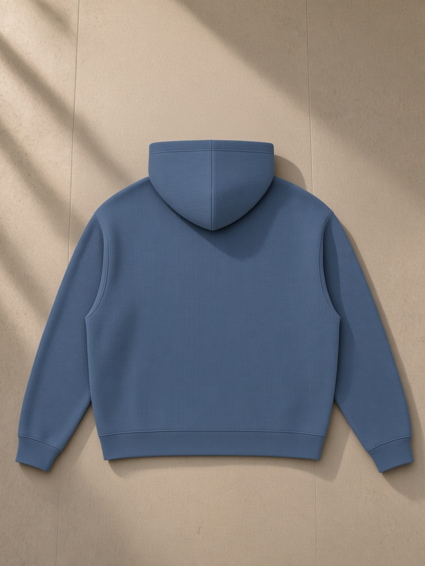 Unisex waffle boxy full zip hoodie in Jeans Blue, laid flat on pale limestone, back view