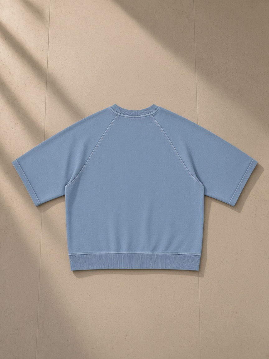 Unisex vintage wash boxy short sleeve sweatshirt in Blue, laid flat on pale limestone, back view
