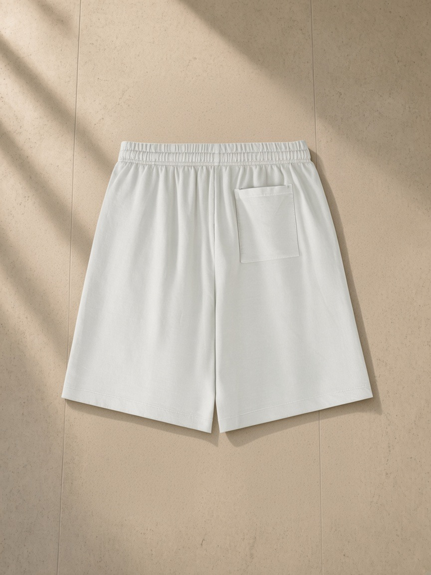 Vintage Wash Cotton Shorts in Greyish White, laid flat on pale limestone, back.