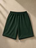 Raw edge fleece shorts in Dark Green, laid flat on pale limestone