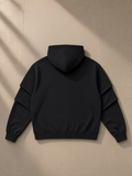 Unisex heavyweight ruched sleeves hoodie in Black, laid flat on pale limestone, back view