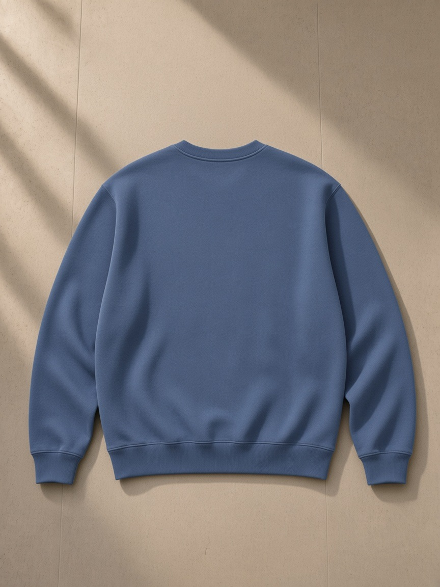 Unisex heavyweight crewneck sweatshirt in Haze Blue, laid flat on pale limestone, back view