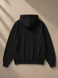 Unisex oversized heavyweight hoodie in Black on a wooden hanger on a wardrobe door in a Tokyo hotel suite over the city lights at night