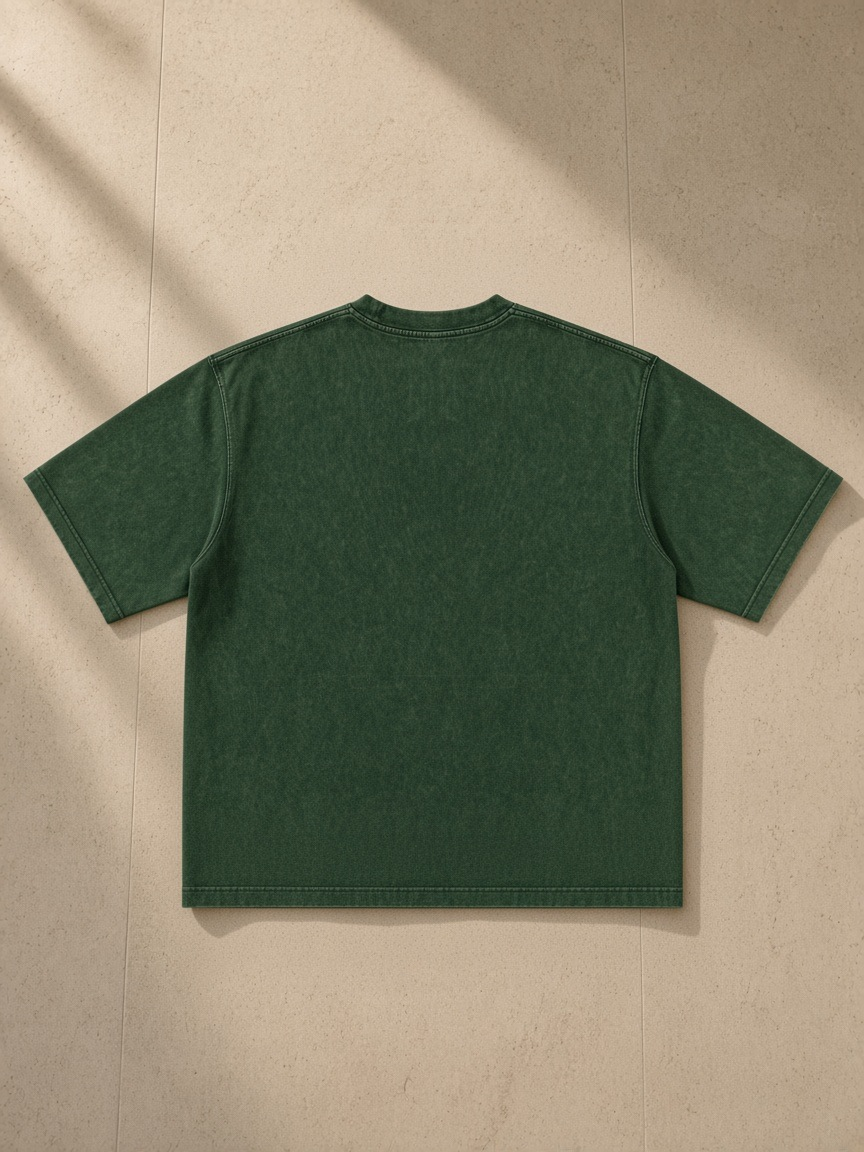 Men's Heavyweight Mineral Wash Boxy T-Shirt in Dark Green, laid flat on pale limestone, back view