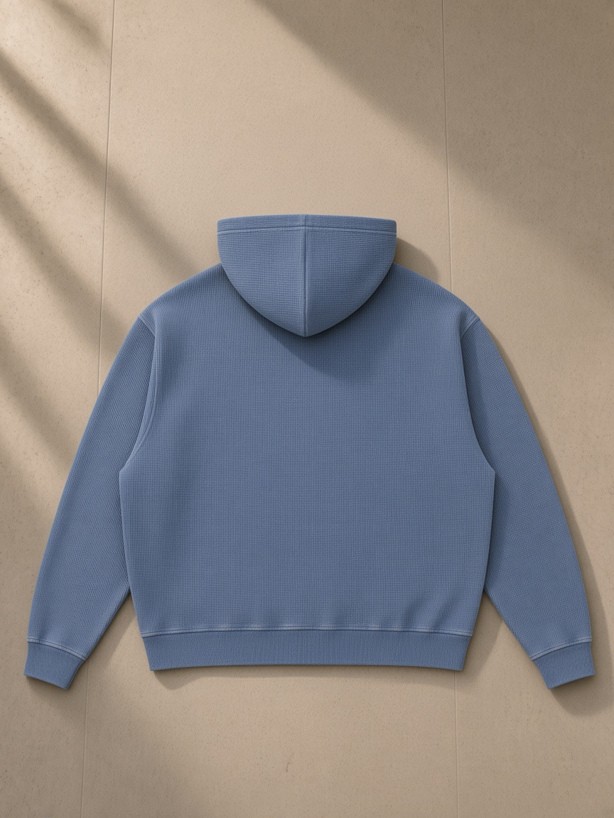 Unisex vintage wash boxy waffle full zip hoodie in Jeans Blue, laid flat on pale limestone, back view