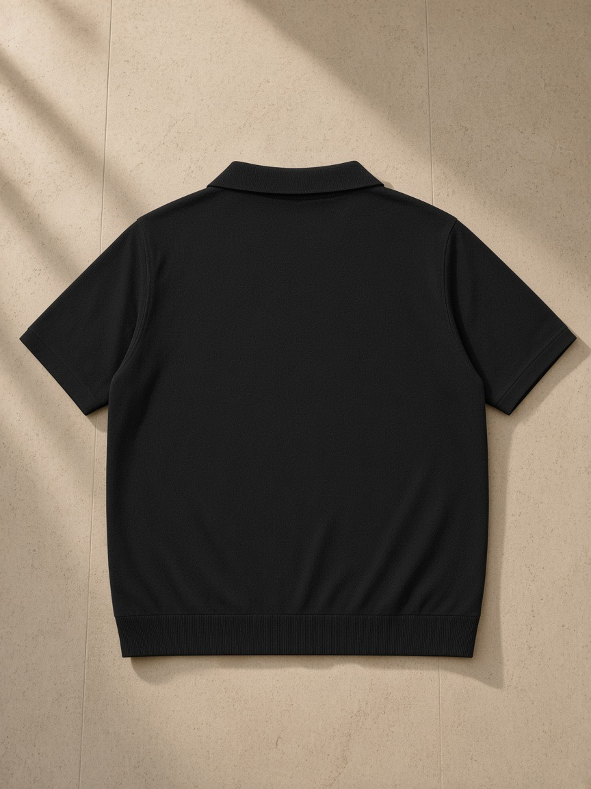Heavyweight Oversized Polo in Black, laid flat on pale limestone, back view