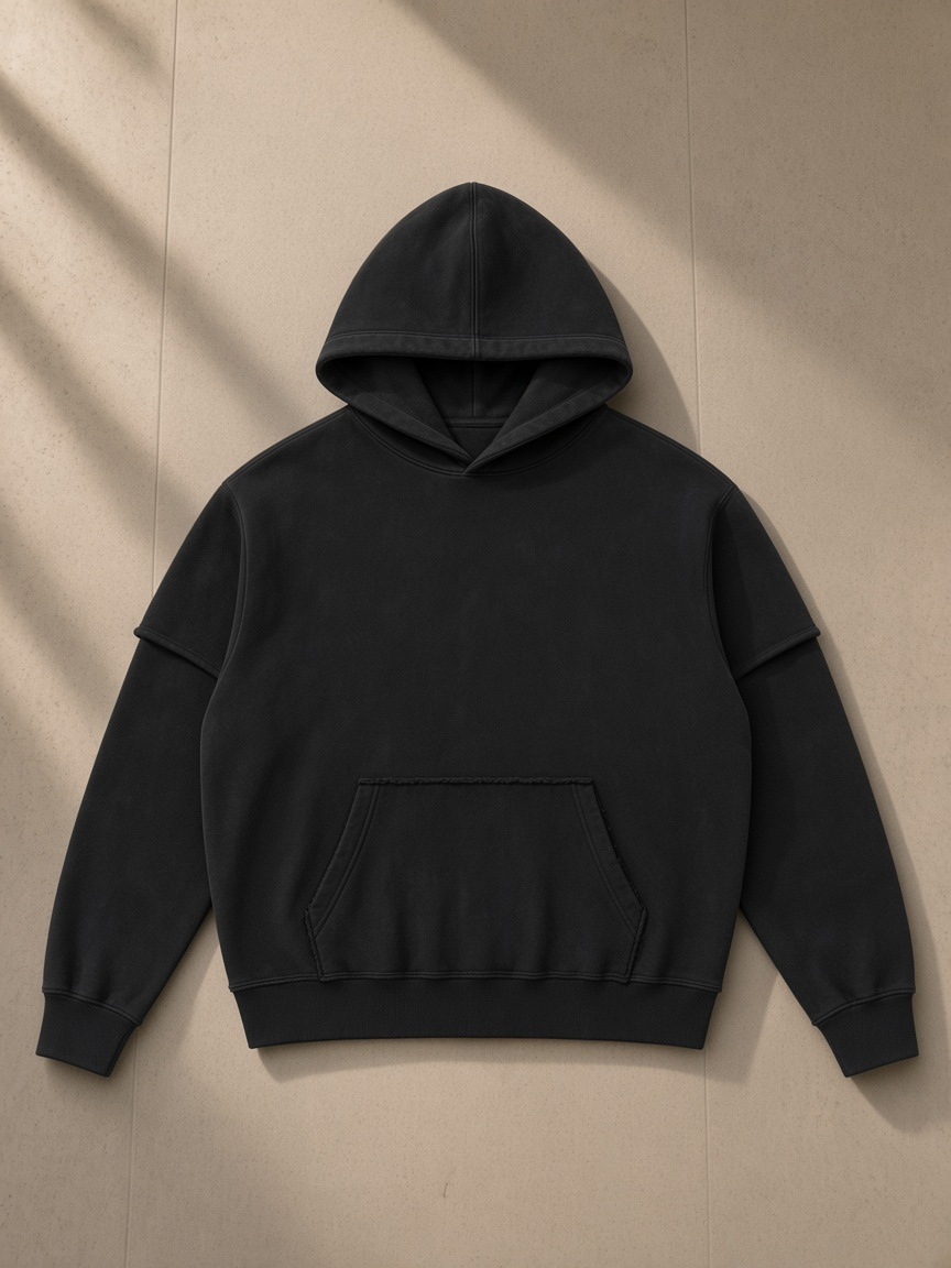 Snow washed raw edge double layered hoodie in Black, laid flat on pale limestone