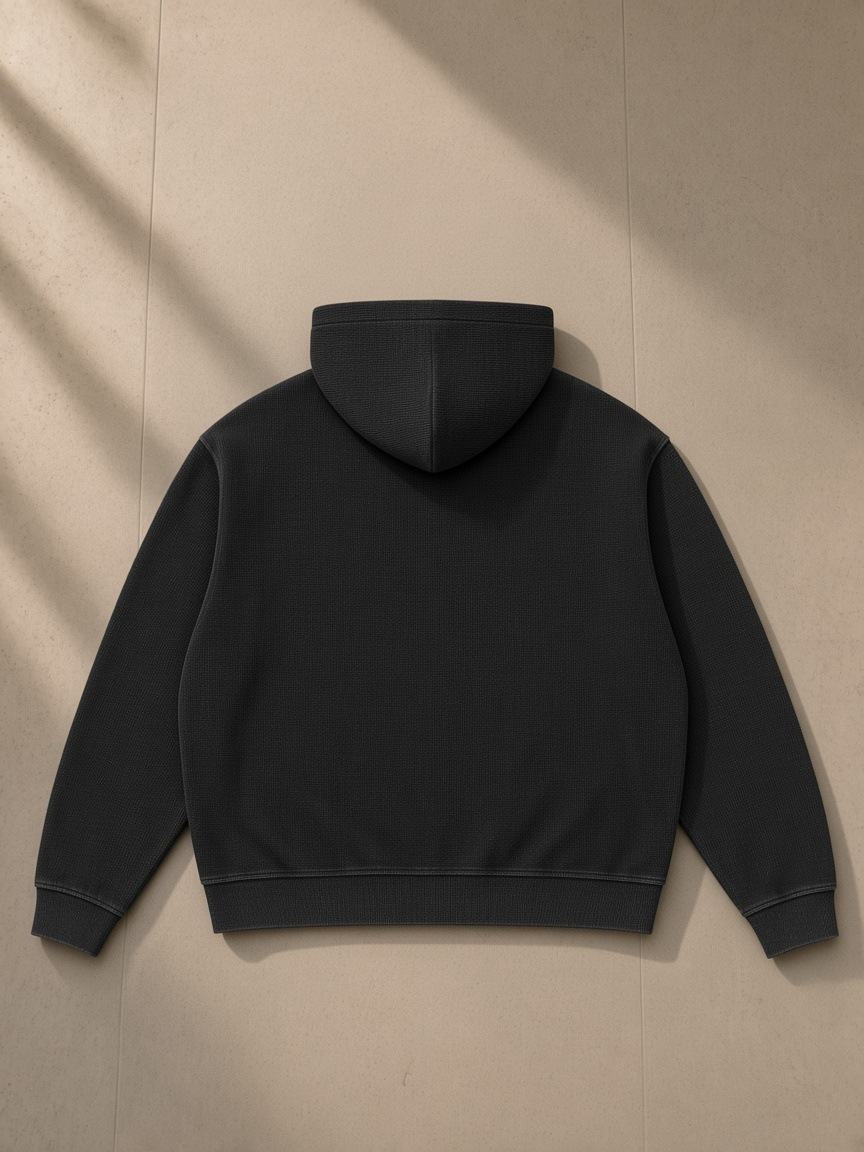 Unisex vintage wash boxy waffle full zip hoodie in Black, laid flat on pale limestone, back view