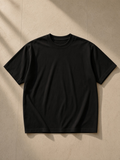 Unisex classic loose boxy tee in Black, laid flat on pale limestone
