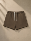Unisex fleece drawstring sweatshorts in Brown, laid flat on pale limestone