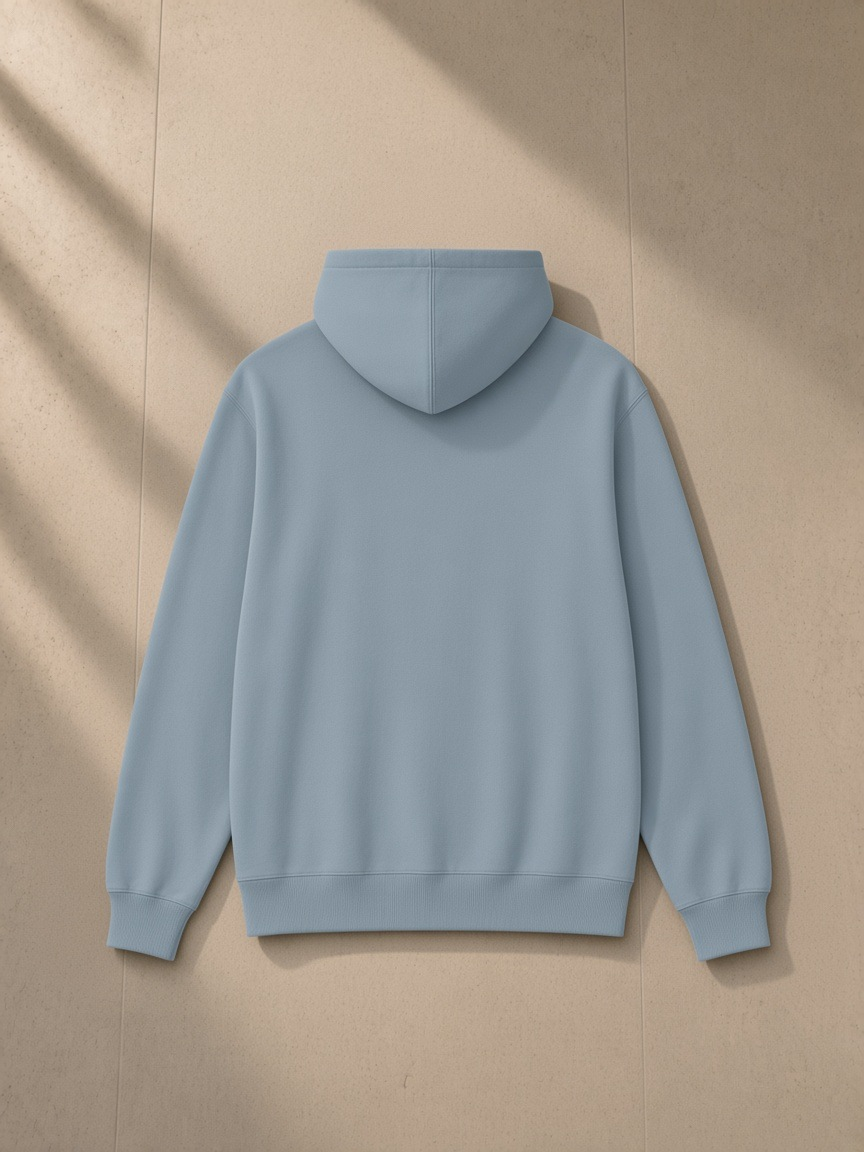 Unisex classic cotton hoodie in Haze Blue, laid flat on pale limestone, back view