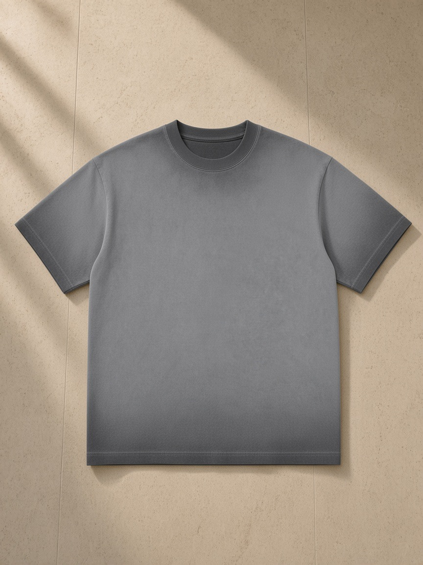 Reverse dyed loose cotton t-shirt in Dark Gray, laid flat on pale limestone