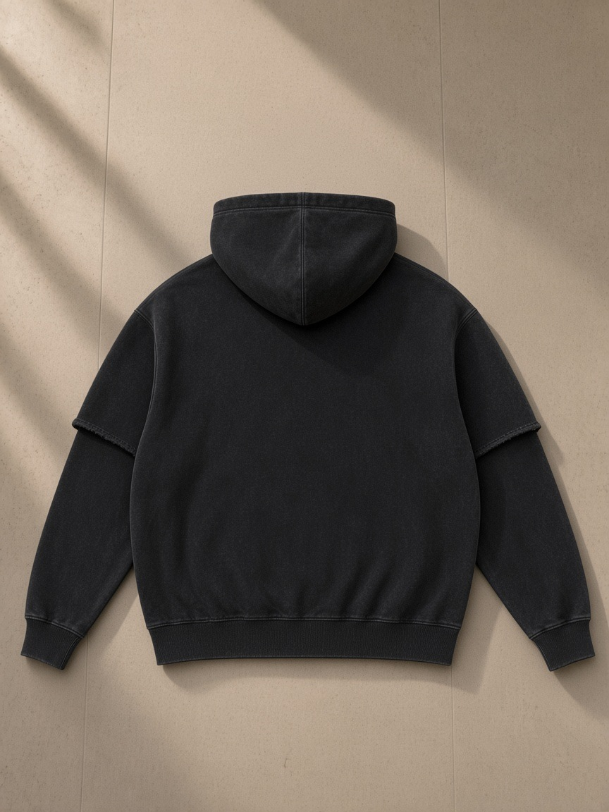 Snow washed raw edge double layered hoodie in Black, laid flat on pale limestone, back view