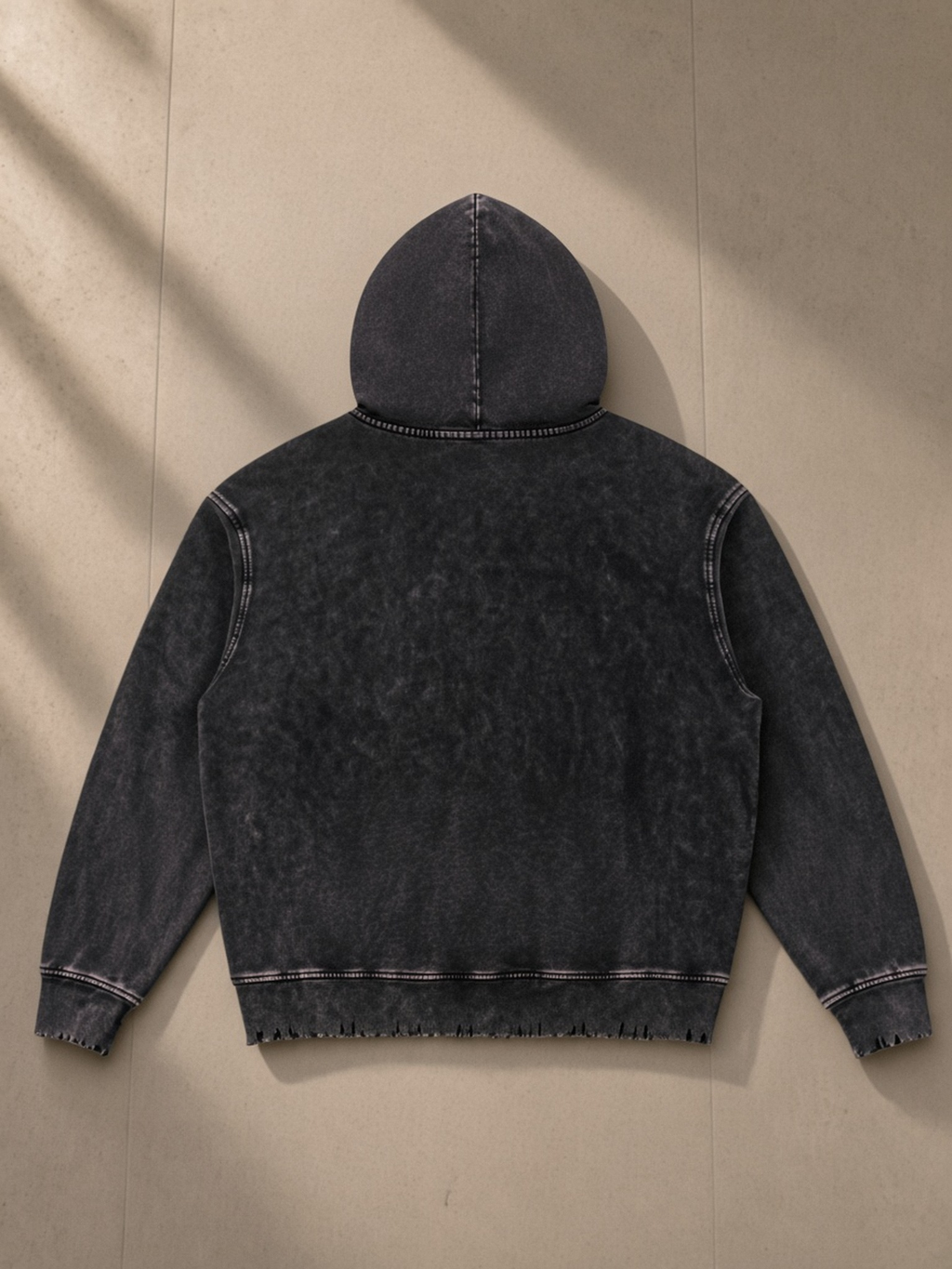 Snow Wash Hand-Frayed Heavyweight Hoodie in Black, laid flat on pale limestone, back.