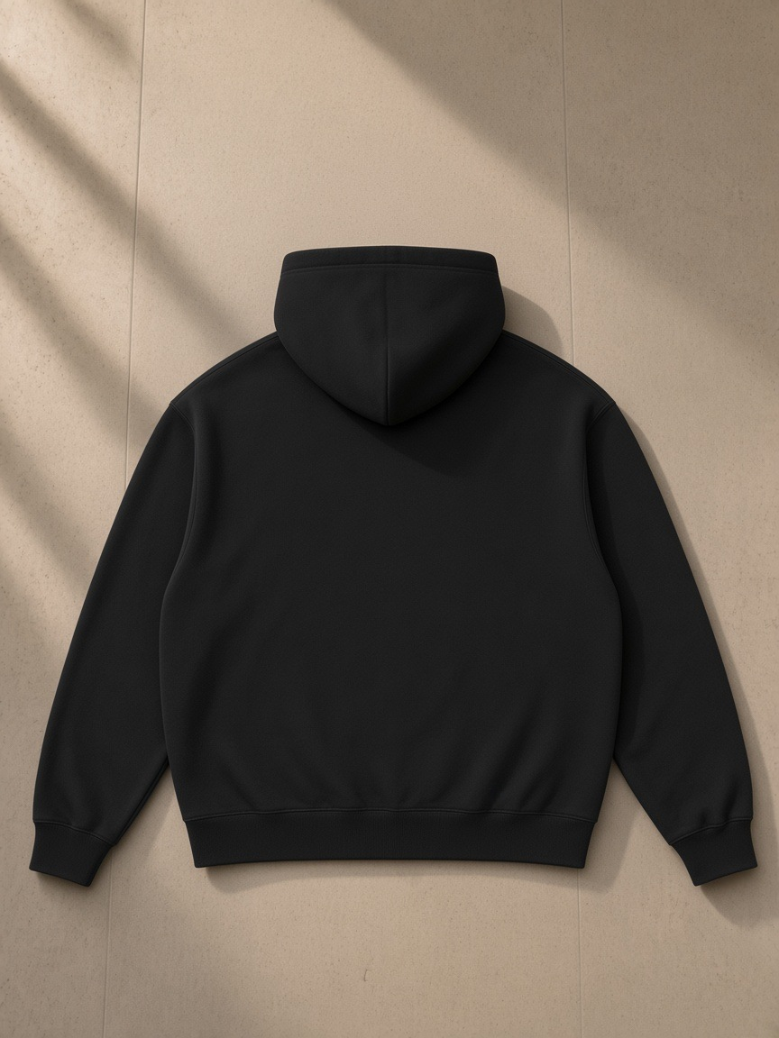 Essential heavyweight hoodie in Black, laid flat on pale limestone, back view