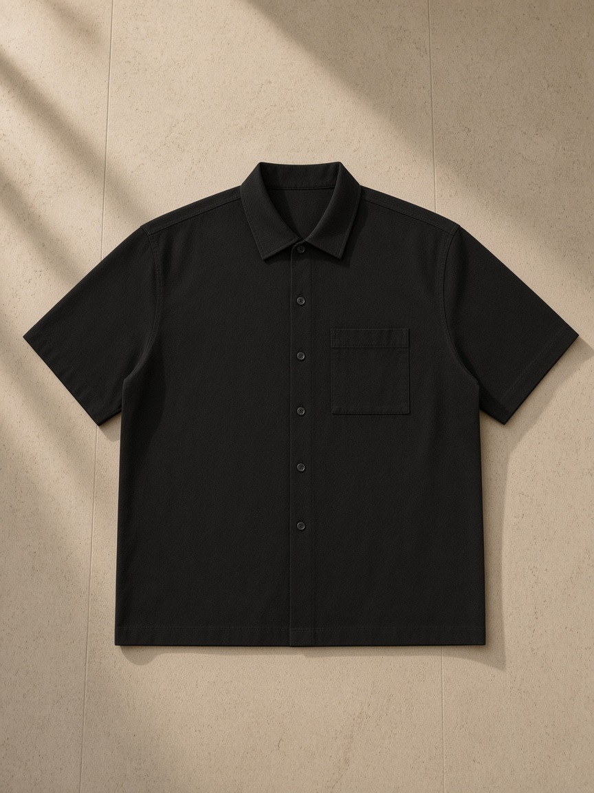 Boxy patch pocket short sleeve shirt in Black, laid flat on pale limestone
