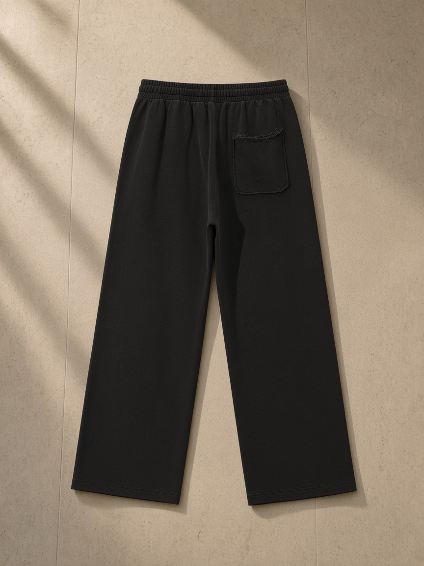 Snow Washed Raw Edge Sweatpants in Black, laid flat on pale limestone, back.