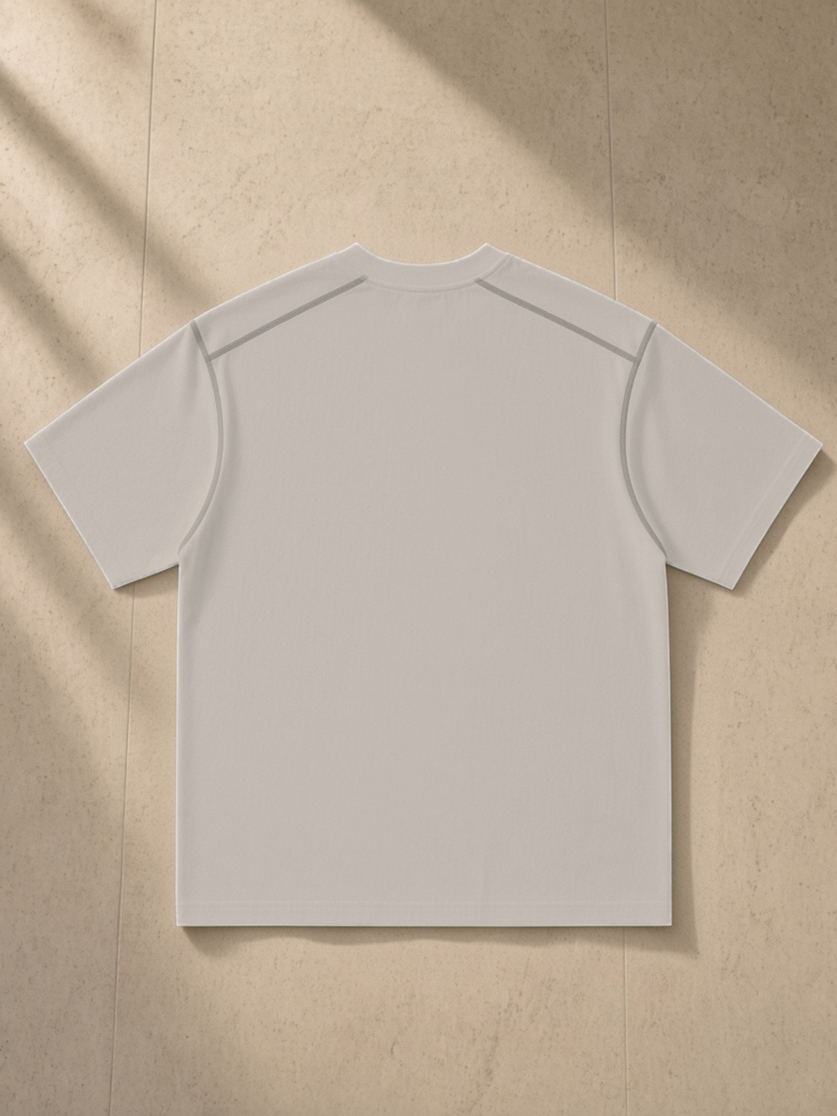 Oversized Contrast-Stitched Cotton Tee in Beige Camel, laid flat on pale limestone, back.