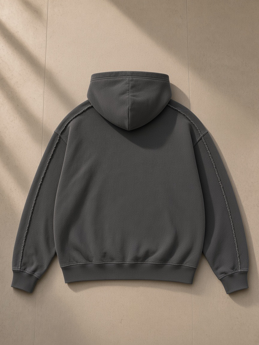 Unisex snow washed tape raw edge zip hoodie in Dark Gray, laid flat on pale limestone, back view