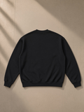 Oversized drop shoulder crewneck sweatshirt in Black, laid flat on pale limestone, back view