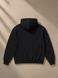 Heavyweight pullover hoodie in Black, laid flat on pale limestone, back view
