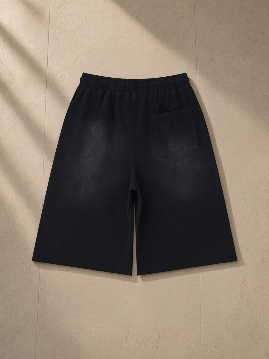 Unisex sunfade raw edge shorts in Black, laid flat on pale limestone, back view