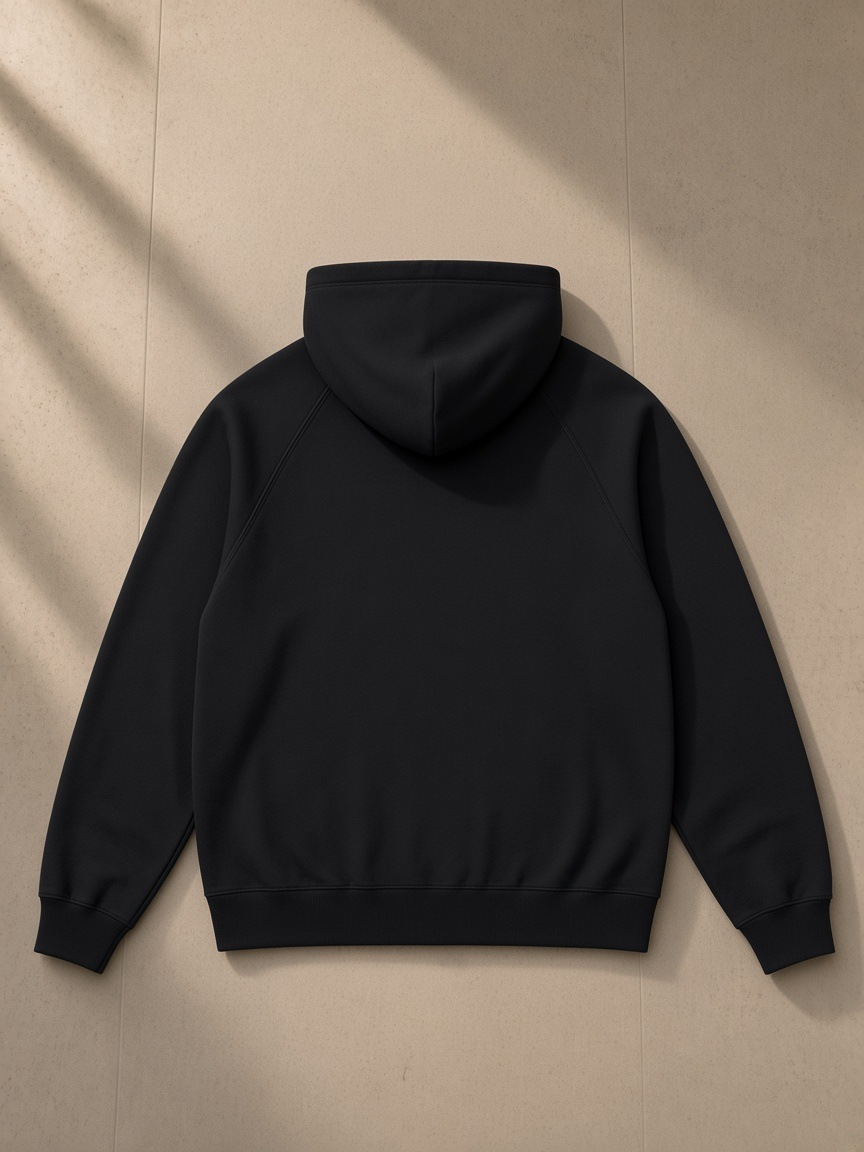 Oversized Raglan Pullover Hoodie in Black, laid flat on pale limestone, back view