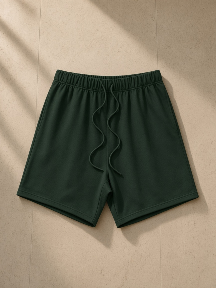 Earth Tone Loose Fit Cotton Shorts in Blackish Green, laid flat on pale limestone