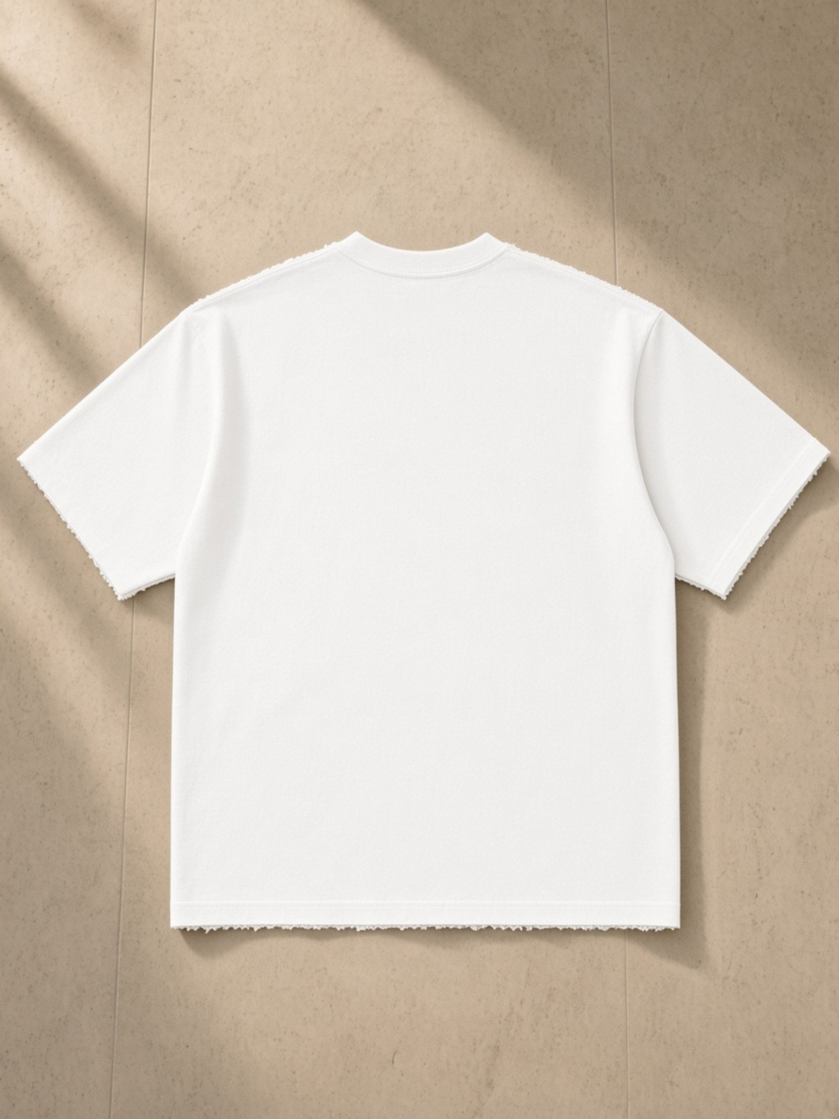 Heavyweight Hand-frayed T-Shirt in White, laid flat on pale limestone, back.