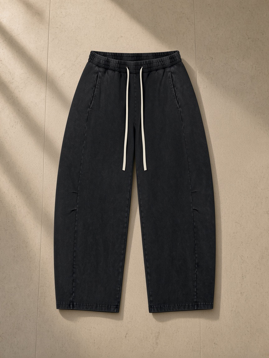 Unisex mineral wash barrel leg pants in Black, laid flat on pale limestone