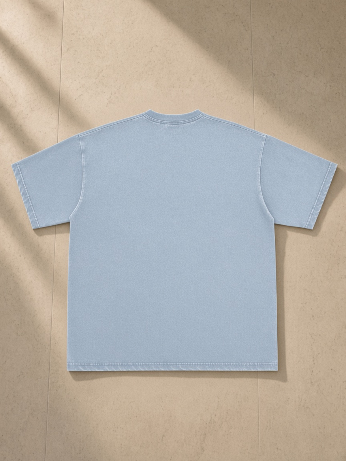 Snow Washed Raw-Edge Neckline T-Shirt in Blue, laid flat on pale limestone, back.