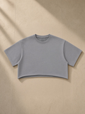 Unisex snow washed raw edge crop top in Gray, laid flat on pale limestone
