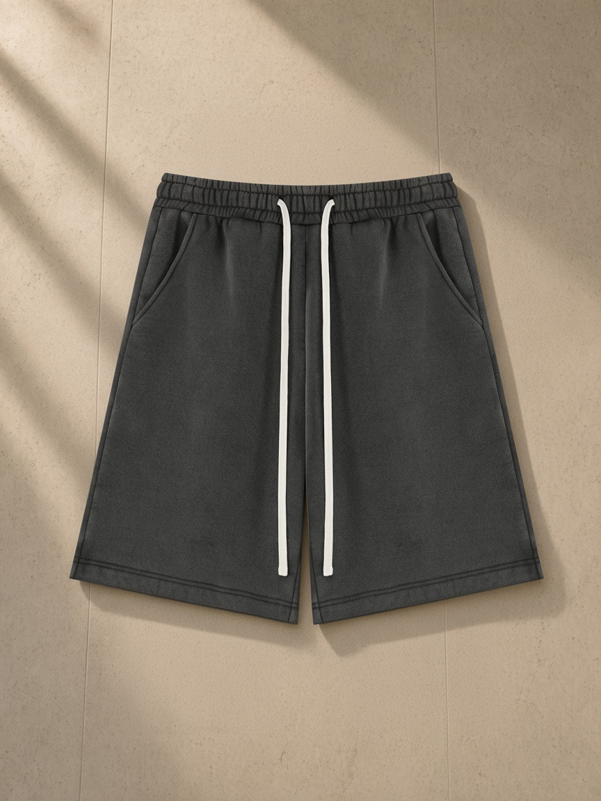 Unisex vintage wash fleece shorts in Black, laid flat on pale limestone