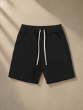 Essential Cotton Shorts in Black, laid flat on pale limestone