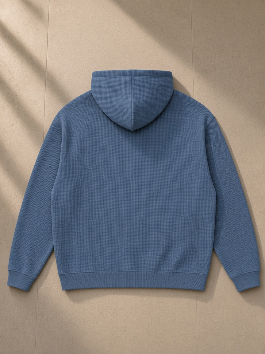 Waffle Hoodie in Jeans Blue, laid flat on pale limestone, back view