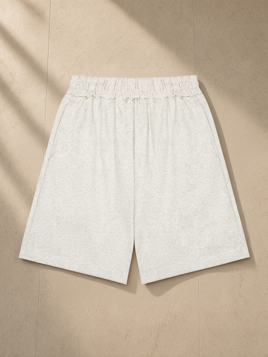 Unisex heavyweight shorts in Oat Gray, laid flat on pale limestone