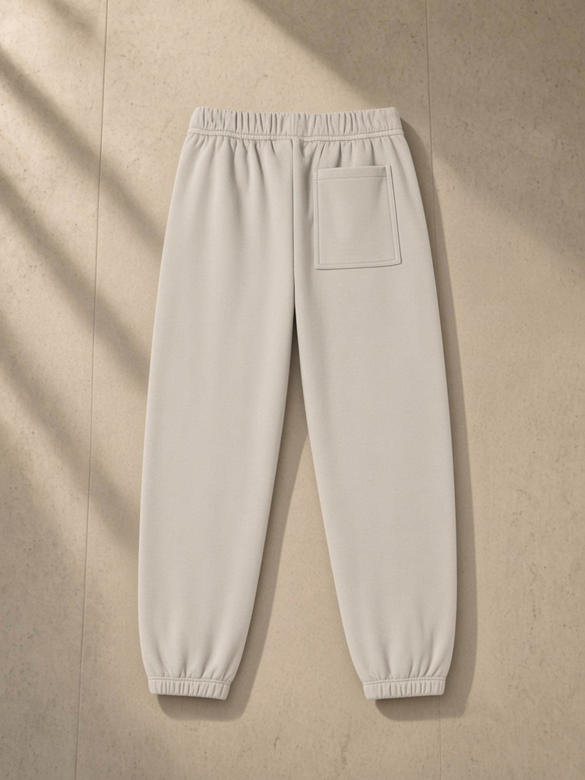 Essential Fleece Sweatpants in Oat Gray, laid flat on pale limestone, back.