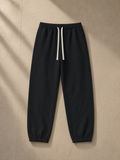 Essential Heavyweight Cotton Sweatpants in Black, laid flat on pale limestone