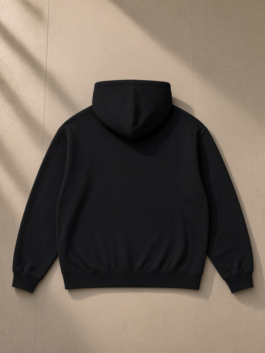 Unisex oversized drop shoulder hoodie in Black, laid flat on pale limestone, back view