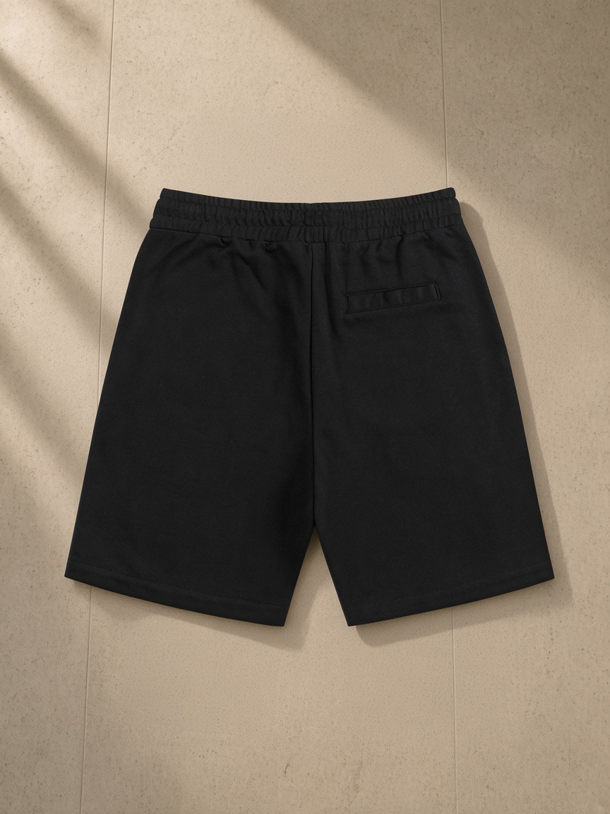 Essential Cotton Shorts in Black, laid flat on pale limestone, back view
