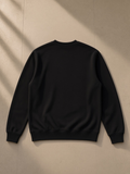 Unisex heavyweight crewneck sweatshirt in Black, laid flat on pale limestone, back view