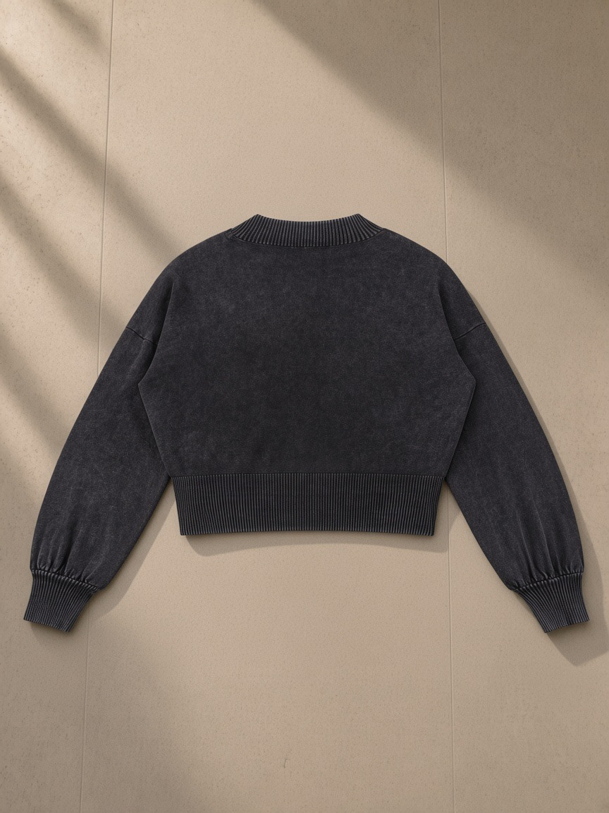 Women's Balloon Sleeve Cropped Sweater in Black, laid flat on pale limestone, back view